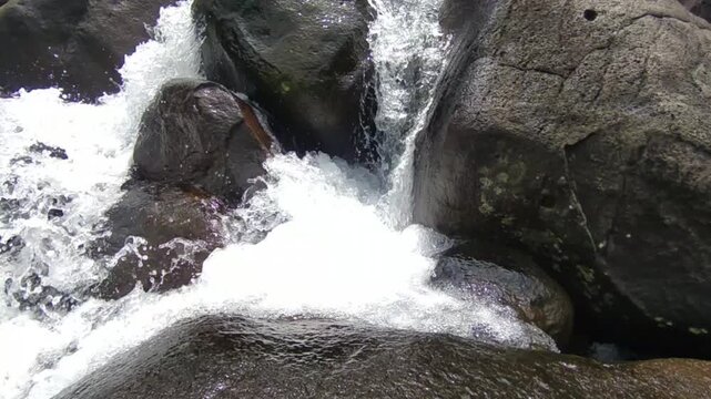waterfall over black rocks close up with fast flowing white water in mountain stream natural background for wellness and travel design