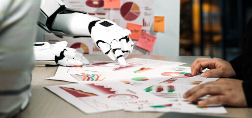 A human and a robot collaborate in a modern office, analyzing data represented in colorful charts and graphs, showcasing innovative technology in teamwork.Noogenesis
