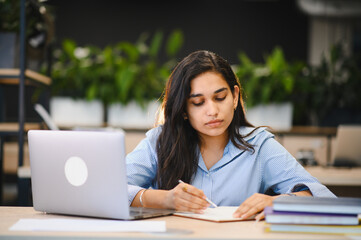 Indian student studying using laptop and writing notes