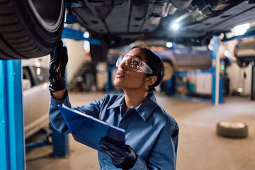Female mechanic inspecting chassis in auto repair shop.