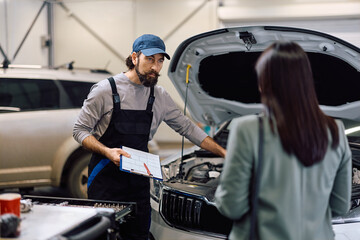 Auto repairman talking to his customer while examining vehicle breakdown in workshop.