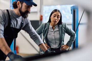 Mid adult woman and her mechanic examining car engine in garage.