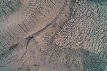Abstract gray soil texture of industrial wasteland with deep erosion channels and dry clay cracks, desolate earth background aerial top down view