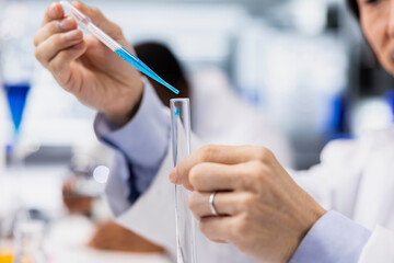 Close up of molecular biologist using pipette to transfer liquid into test tube containing solution at laboratory bench. Research lab worker does pipetting procedure with dropper and sample