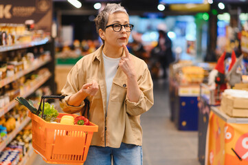 Mature woman thinking while choosing products in supermarket aisle