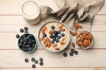 Tasty oatmeal with almond milk, nuts and blueberries on wooden table, flat lay