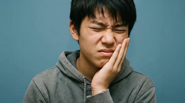 耐えがたい歯の痛みに襲われ、頬を押さえて苦悶の表情を浮かべる若い男性