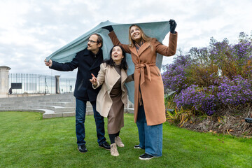 Friends having fun under a blanket on a cloudy day in a park