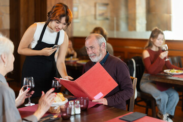 Obraz premium Polite young waitress taking order from elderly couple during relaxed dinner in comfortable restaurant setting