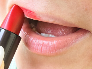 A woman paints her lips with red lipstick, a natural process.
