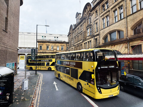 Manchester UK yellow double decker buses on a historic street with architecture and city life