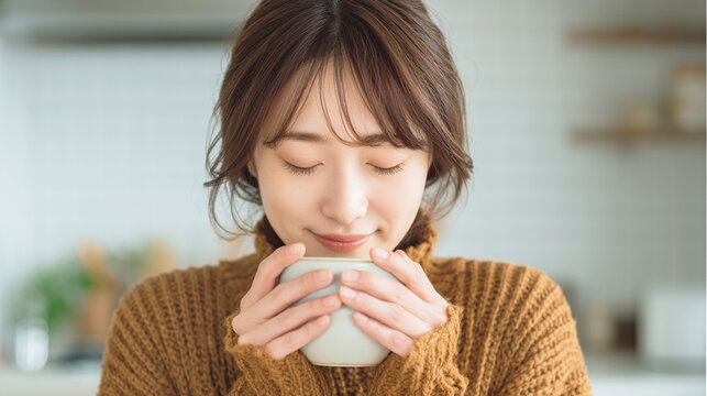 温かい飲み物の入ったマグカップを両手で持つ女性
