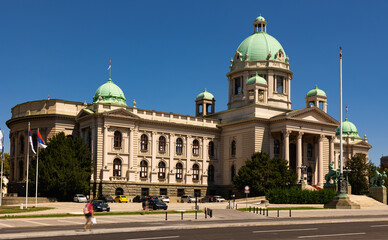 Naklejka premium Scenic view of Neoclassical building of National Assembly of Serbia in Belgrade with green domes, classical columns, and bronze horseman sculptures captured on clear summer day