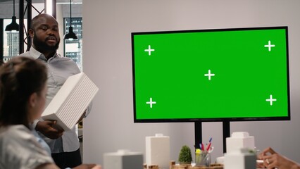 Property engineers team study architectural blueprints with a mockup on TV, collaborating in urban development master plan. Modern residential project with infrastructure goals.