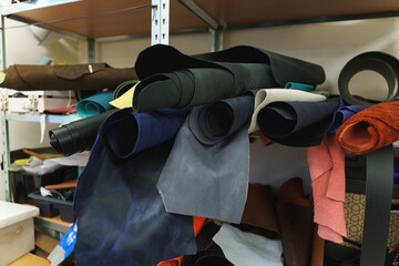 Stacked pieces of genuine leather in black and brown shades showing natural textures in a workshop.