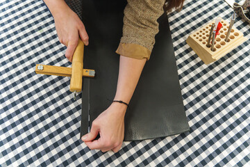 Leather artisan using a wooden strap cutter to slice precise strips from a black leather sheet.
