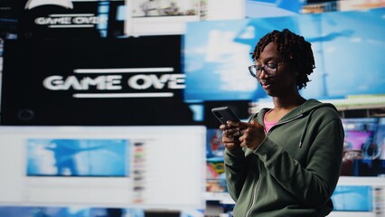 Cheerful young woman using mobile phone to browse internet, looking at surrounded by videos. Smiling african amercian teenager enjoying free time browsing online clips on smartphone, camera A