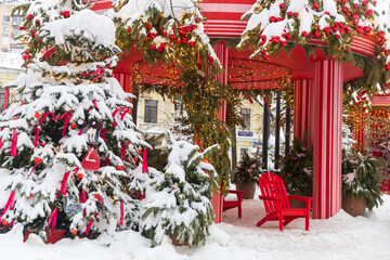 Red and white striped pavilion decorated with red baubles and lights next to a snowy Christmas tree in Moscow, Russia.