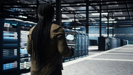 Data center engineer using deep learning on laptop to optimize operations efficiency. IT expert working in server room with specialized hardware accelerating complex AI calculations, camera A