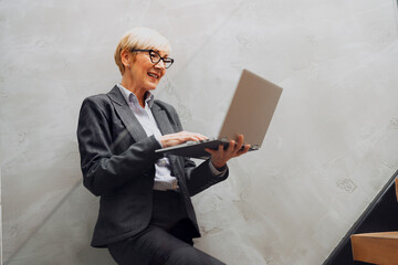 A professional middle-aged blonde businesswoman having a video call on her laptop in a bright office