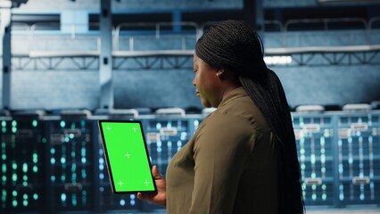 Data center specialist monitors data center metrics on green screen tablet to enhance operational effectiveness. Server room worker uses analytics on chroma key device to predict performance, camera B