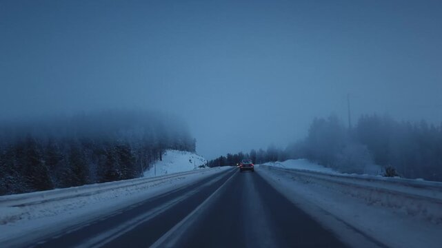 Car is driving on a frozen road in ice. Driver drives a car on a snowy highway in winter. Polar night in Arctic pine forest. Cold weather. Blizzard in winter journey, outdoor. Snowstorm in road trip.