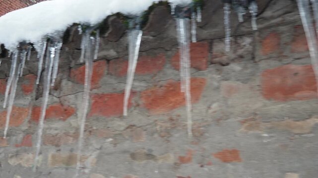 Icicles dangle from snow-covered rooftop. Glistening forms contrasting with rustic charm of old brick wall. Witness winter beauty and delicate balance of nature. Freezing of dripping or flowing water