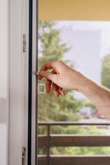 A hand is seen locking a plastic window frame in a residential apartment