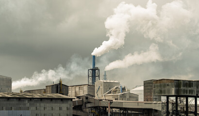 Industrial plant with smoking chimneys under a cloudy sky. Industrial factory landscape representing manufacturing, pollution, and global warming