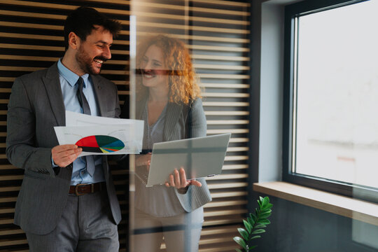 Businessman and businesswoman analyzing financial results on papers and using a laptop, professional colleagues discussing data in the office - Powered by Adobe
