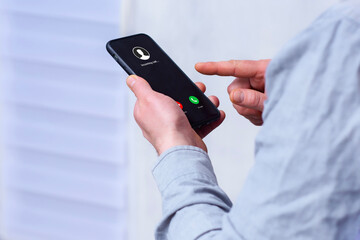 Hand holding modern black smartphone displaying incoming call screen with Accept green and Decline...