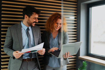 Businessman and businesswoman analyzing financial results on papers and using a laptop, professional colleagues discussing data in the office