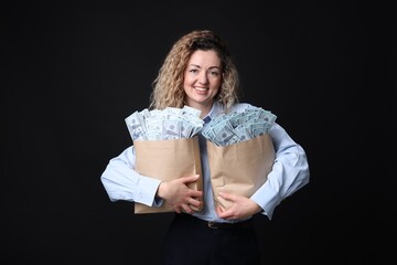 Happy businesswoman with bags full of money on black background