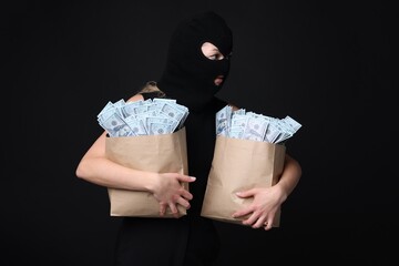Masked thief with bags full of money on black background