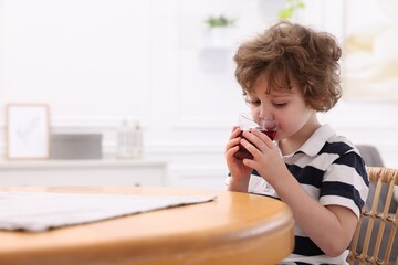 Little boy drinking fresh pomegranate juice at table indoors. Space for text