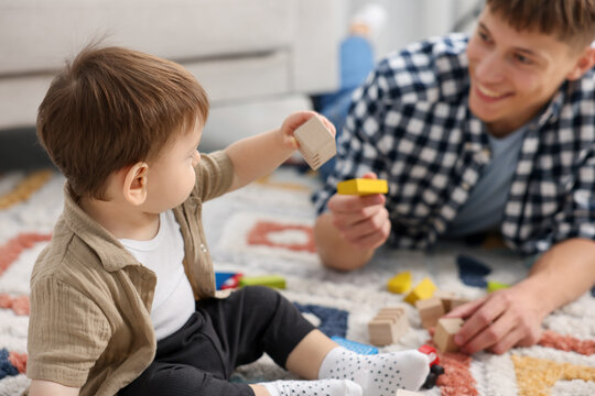 Smiling male nanny and cute little boy playing with toys on floor at home, selective focus