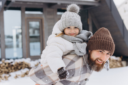 Father carrying happy daughter piggyback in winter snow