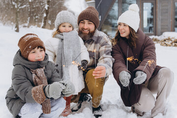 Family celebrating winter holidays with sparklers in snow