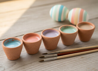 Pastel paints in tiny clay pots with paintbrushes. Easter egg decoration for creative hobby. Spring craft activity kit for holiday.