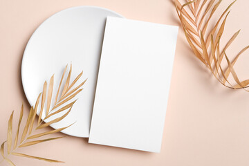Blank wedding menu card mockup on a round white plate with elegant dried palm leaves, showcasing a minimalist design with ample copy space for customization and personalization