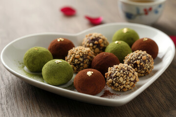 Macro view of assorted chocolate truffles on a heart-shaped dish, highlighting rich textures and warm, festive Valentine atmosphere.