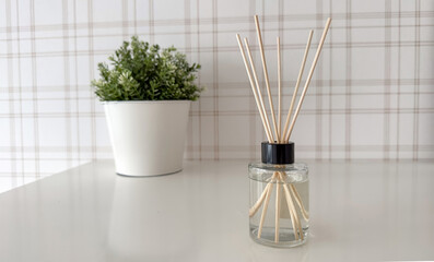 A minimalist home decor composition featuring a clear glass reed diffuser bottle with wooden sticks standing on a glossy white table