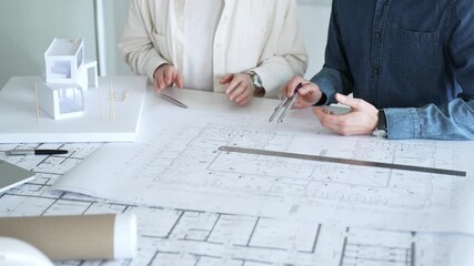 Engineering professionals collaborating on an architectural blueprint, using a compass to design a modern building, planning construction with a house model and laptop