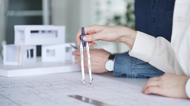 Architects collaborating on blueprint plans, discussing engineering details and project designs, planning construction development with a laptop in a modern office environment
