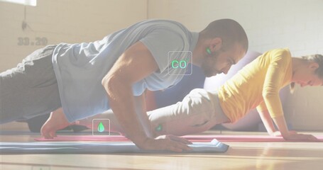 Holding high plank, male in light blue t-shirt exercising in studio with mats, tablet, CO2 overlay