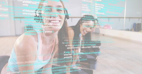 Leaning forward five women in sportswear laughing on exercise mats in studio, code overlay