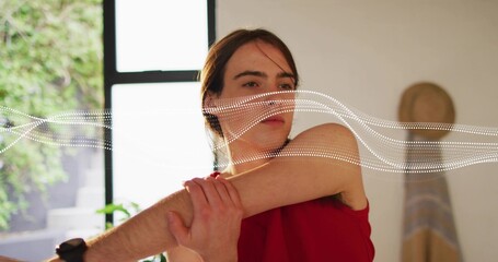 Stretching woman wearing red tank top pulling elbow across chest at home, waveform overlay visible
