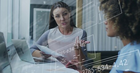 Gesturing light-top woman holding papers blue-top peer taking notes at office with laptop, glass UI