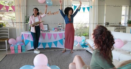 Celebrating pregnant mom raising arms at home baby shower, with denim top, rust skirt and balloons