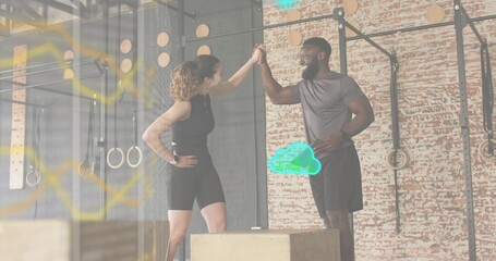 High-fiving workout partners wearing athletic clothing in warehouse gym, with plyo boxes and rig